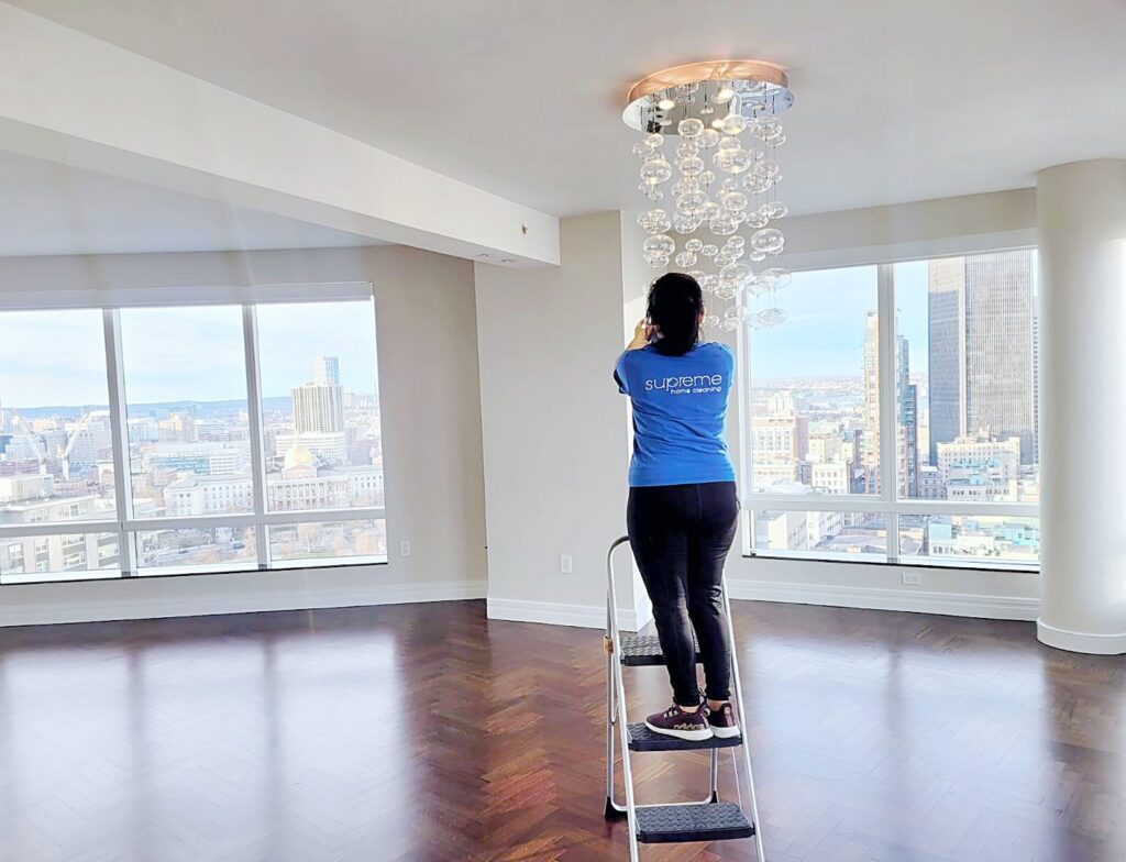 A professional cleaner from Supreme Home Cleaning, Inc wiping a chandelier in a modern apartment in Boston, MA.