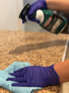 A cleaner wearing purple gloves spraying and wiping a kitchen countertop, showcasing house cleaning by Alma's Cleaning Services in Sacramento, CA.