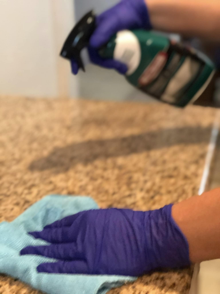 A cleaner wearing purple gloves spraying and wiping a kitchen countertop, showcasing house cleaning by Alma's Cleaning Services in Sacramento, CA.