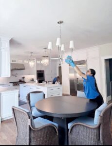 A house cleaner from Supreme Home Cleaning, Inc wiping a dining room chandelier in a clean home in Boston, MA.
