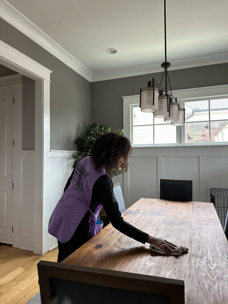 A professional cleaner wiping down a large wooden dining table for Sunshine Cleaning & Painting in Raleigh, NC.