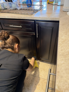 A house cleaner in uniform wiping down kitchen cabinets near the floor with a yellow cloth for Eco-Terra Clean in Fort Lauderdale, FL.