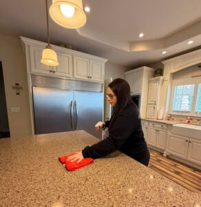 A professional cleaner wiping down a kitchen counter with a red cloth and spray bottle for Home Clean Home By Maria LLC in Aberdeen, SD.