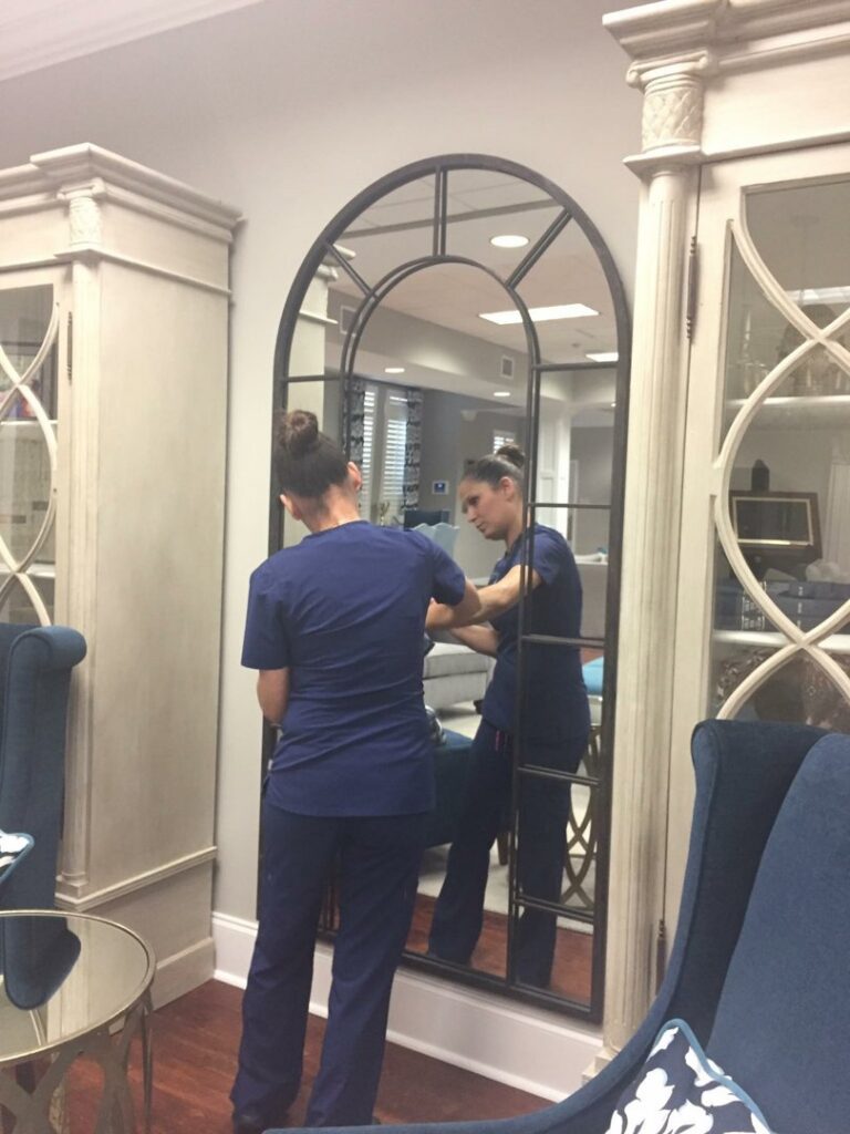A professional cleaner in blue scrubs meticulously wiping a large decorative mirror, provided by Precise Cleaning Solutions in Auburn, AL.