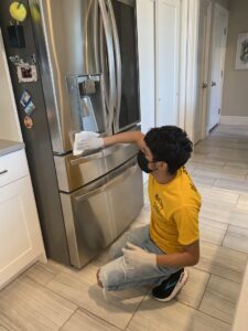 A cleaner from Bivian's Cleaners LLC wiping down a stainless steel refrigerator in Trenton, NJ.
