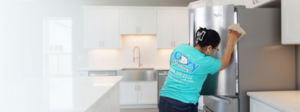 A professional cleaner from Cozy Cleaning VA wiping down a stainless steel refrigerator in a modern kitchen in Richmond, VA.