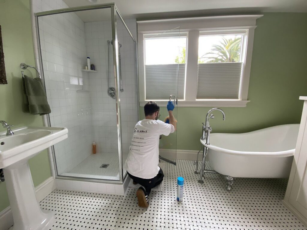 A professional cleaner from Mr. & Mrs. K Cleaning Services LLC wiping down a shower door in a bathroom in Sacramento, CA.
