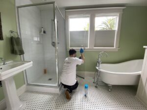 A professional cleaner from Mr. & Mrs. K Cleaning Services LLC wiping down a shower door in a bathroom in Sacramento, CA.