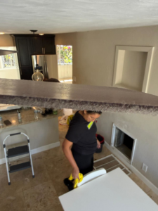 A house cleaner in gloves wiping down a white table in a kitchen area for Eco-Terra Clean in Fort Lauderdale, FL.