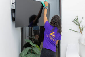 A house cleaner from Ascent Cleaning Solutions, LLC wiping a TV screen in a home in Nashville, TN