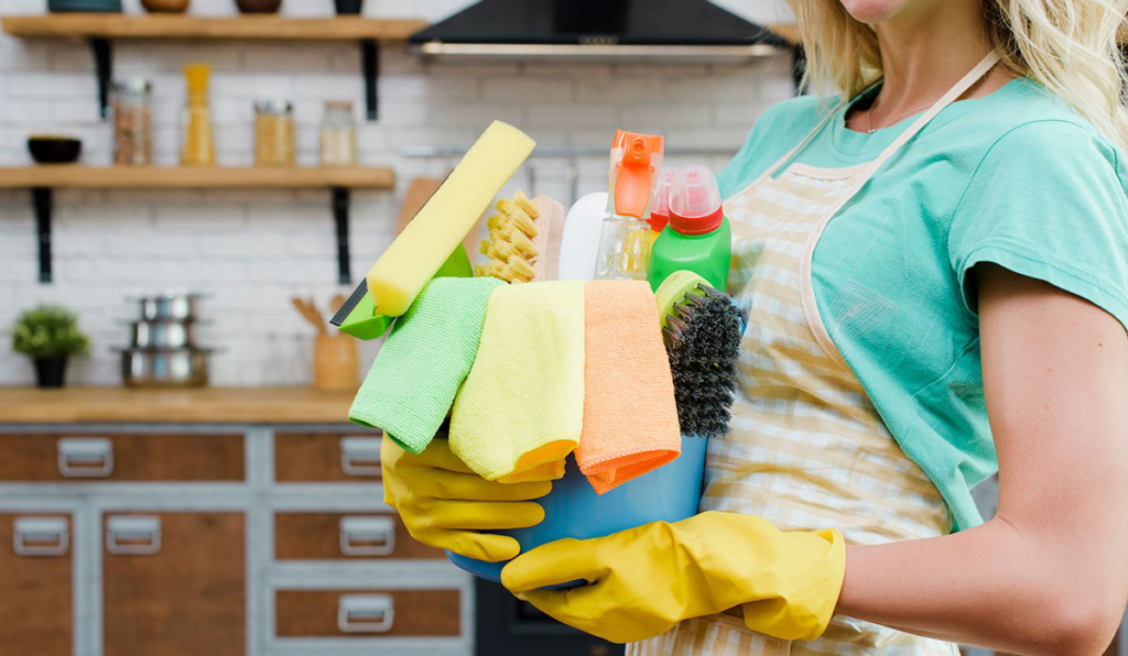 A cleaner holding a bucket full of various cleaning supplies in a modern kitchen for PAP-Cleaning Services in Fort Lauderdale, FL.