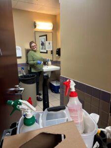 A professional cleaner wearing gloves, standing with a cleaning cart in a restroom at a job site for Crabby Cleaners in Mount Vernon, KY