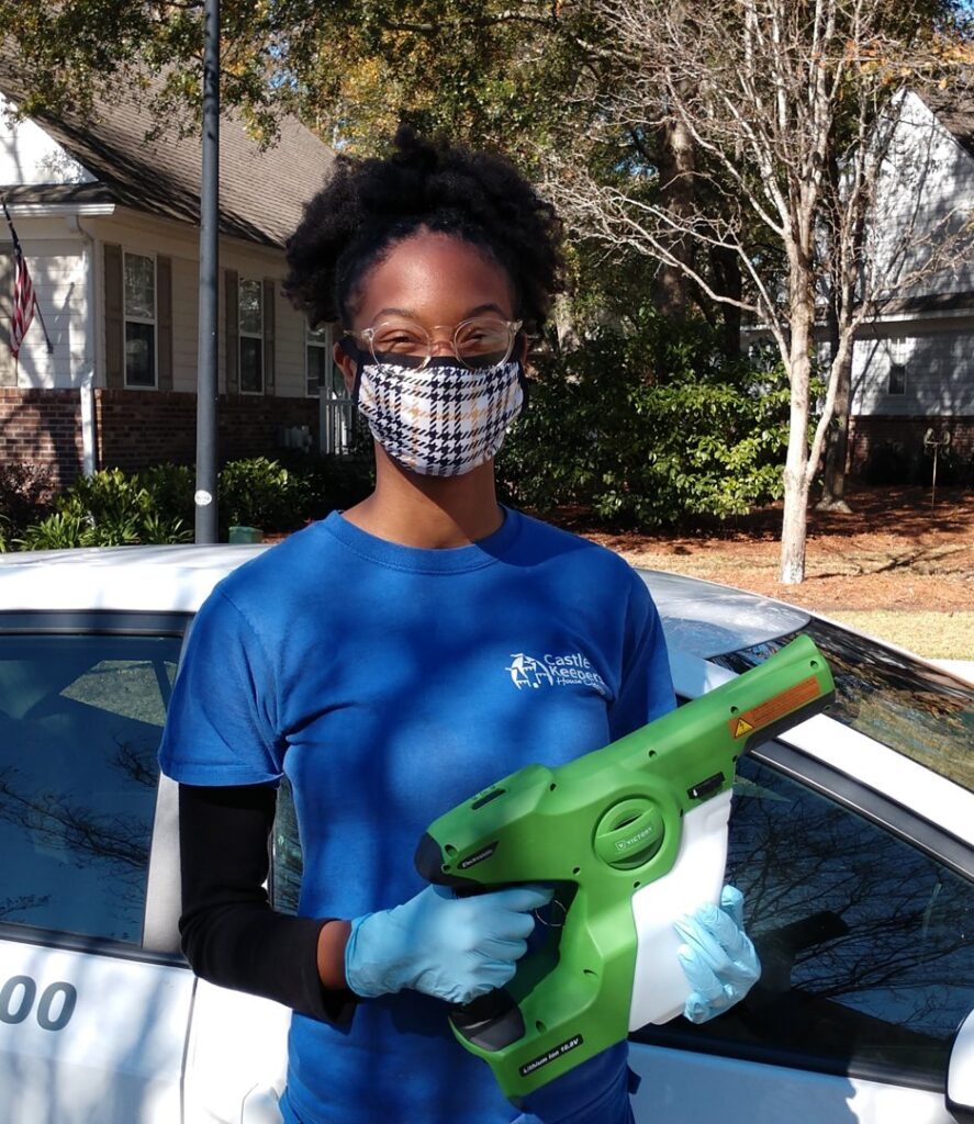 A Castle Keepers House Cleaning professional in North Charleston, SC, wearing a mask and gloves, holding an electrostatic sprayer for advanced sanitization.