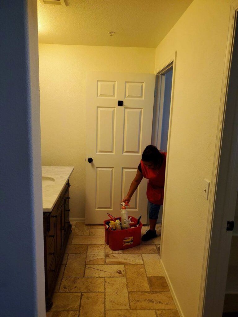 A house cleaner reaching into a red supply caddy in a bathroom doorway for Arizona Housekeeping Service in Phoenix, AZ.