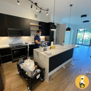 A cleaner wearing a mask and gloves, working in a modern kitchen for The Prime Cleaner in Miami, FL.