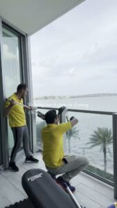 Two professional cleaners washing balcony windows with a water view at The Prime Cleaner in Miami, FL.