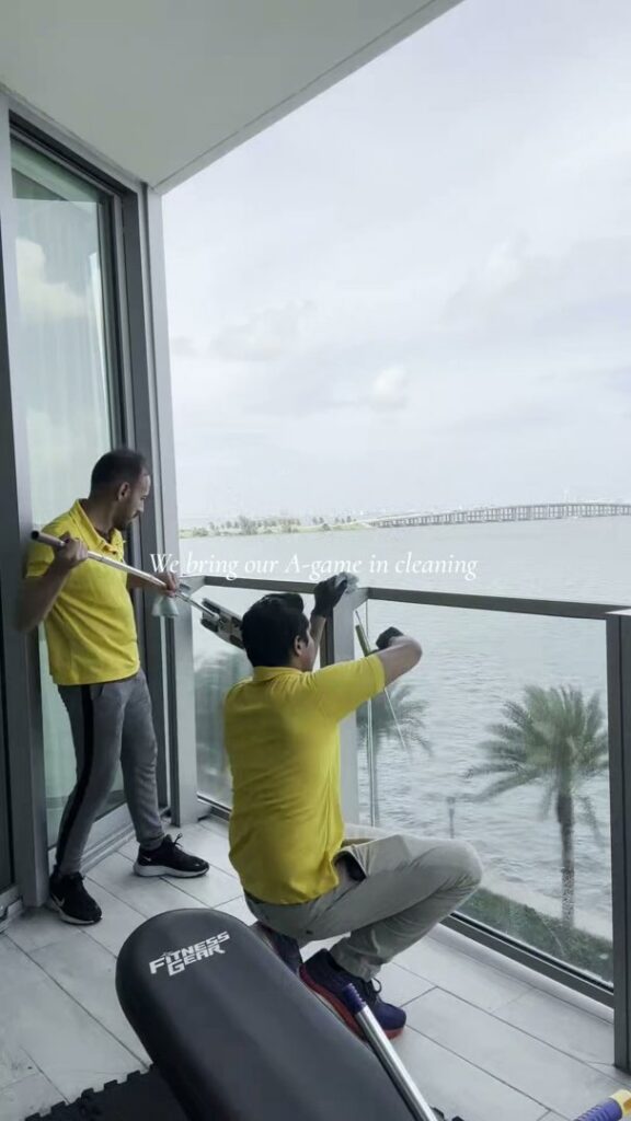 Two professional cleaners washing balcony windows with a water view at The Prime Cleaner in Miami, FL.