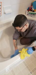 A professional cleaner from Leave The Dust To Me Cleaning Services LLC in Anchorage, AK, thoroughly cleaning a bathtub in a bathroom.