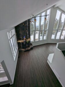 A house cleaner from Leave The Dust To Me Cleaning Services LLC in Anchorage, AK, cleaning a fireplace mantel in a spacious living room.