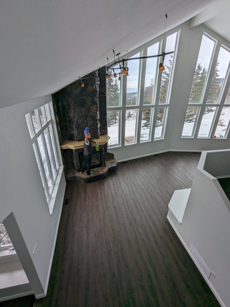 A house cleaner from Leave The Dust To Me Cleaning Services LLC in Anchorage, AK, cleaning a fireplace mantel in a spacious living room.