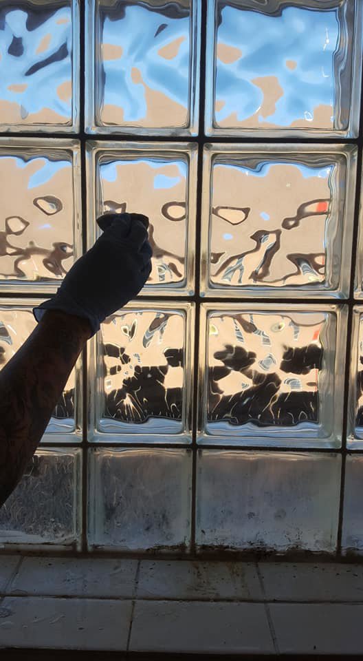 A gloved hand cleaning a glass block window, demonstrating house cleaning services by Jessie Clean in Indianapolis, IN.
