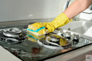 A gloved hand scrubbing a kitchen stovetop with a sponge and suds for All Advanced Tactical Klean LLC in Columbus, OH.