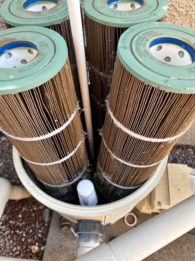 A pool technician cleaning dirty pool filter cartridges with a hose, a service provided by Aloha Pool Cleaning LLC in Las Vegas, NV.