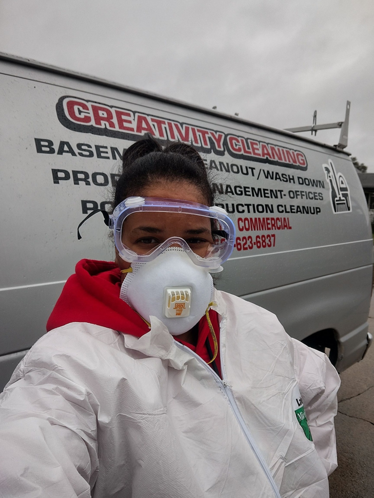 A cleaning professional in protective gear standing in front of a Creativity Cleaning LLC van in Detroit, MI.