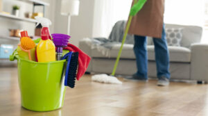 A bucket of cleaning supplies in the foreground with a house cleaner mopping a wooden floor in the background, by ECO Friends cleaning service in Carson City, NV.