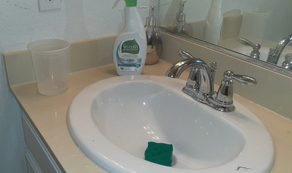 Cleaning supplies, including a spray bottle and sponge, on a bathroom sink by Go Green Cleaning Experts Of NV in Reno, NV