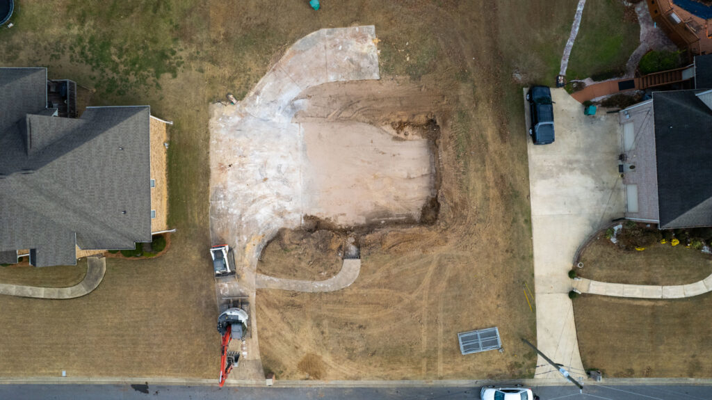 Aerial view of a recently cleared demolition site during cleanup, with an excavator and dump truck from Nuckles Services in Birmingham, AL