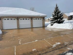 A residential driveway and garage entrance cleared of snow, showcasing snow removal by Medina's Landscape Care LLC in Layton, UT.