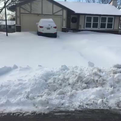 A residential driveway cleared of snow with a large snow bank, showcasing QUIKPLOW's snow removal service in Grand Rapids, MI.