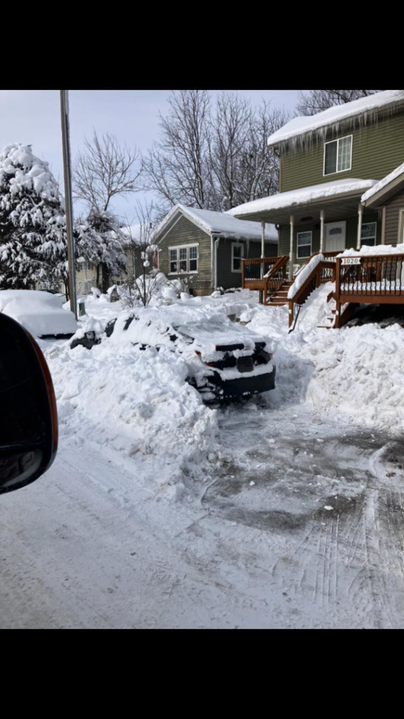 A cleared driveway and path after snow removal by Spindrift Lawn & Snow in Iowa City, IA, with a car still surrounded by deep snow.