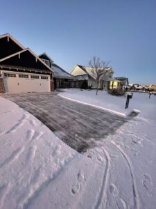 A residential driveway and sidewalk completely cleared of snow by Yard Aesthetics in Edmond, OK, with snow piled on the sides.