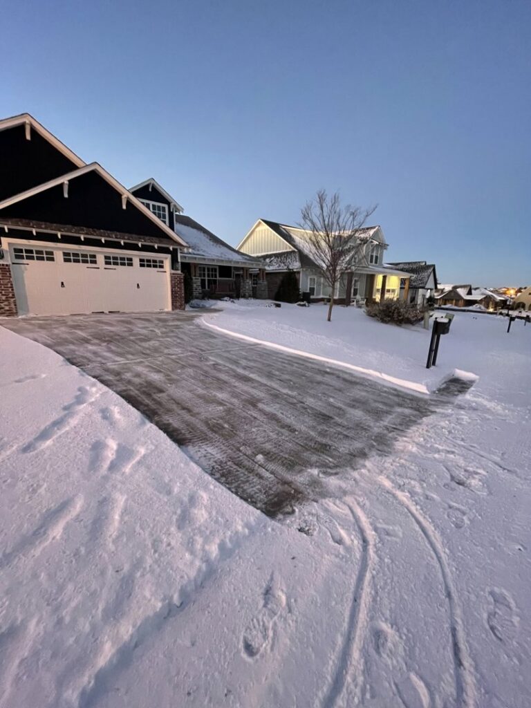 A residential driveway and sidewalk completely cleared of snow by Yard Aesthetics in Edmond, OK, with snow piled on the sides.