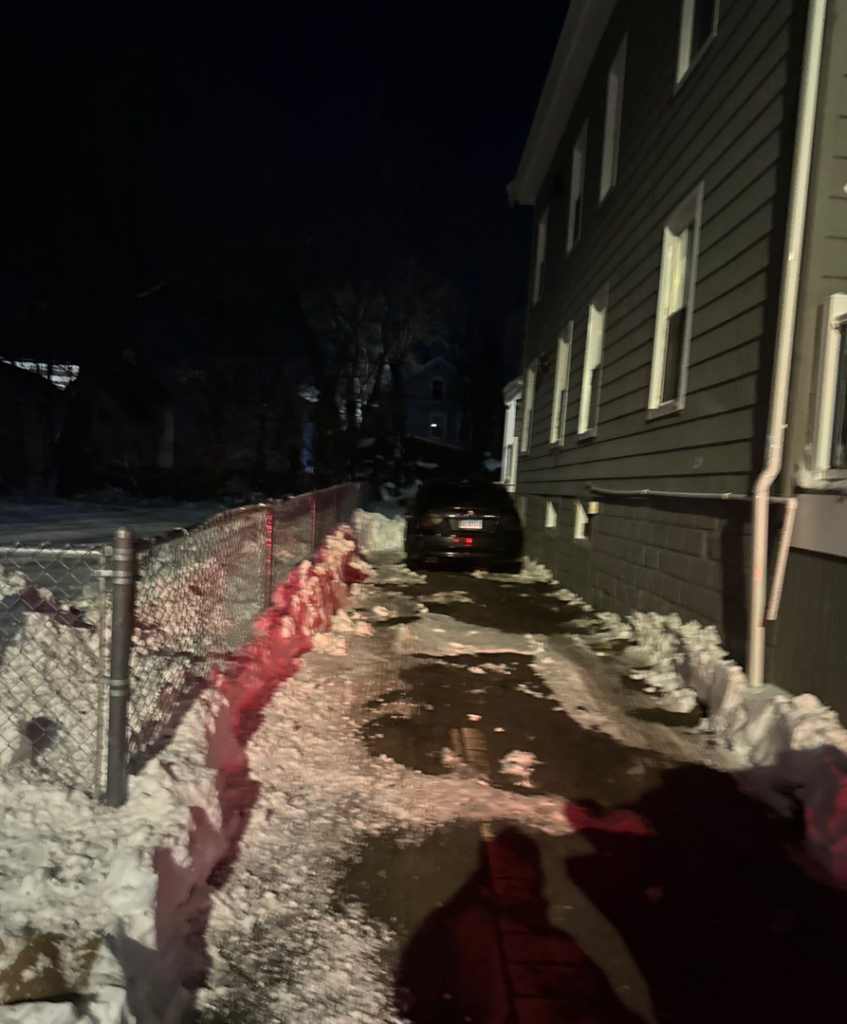 A residential driveway cleared of snow at night, showing a wet path and snow piles, by Diamond Image in New Haven, CT.