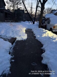 A residential sidewalk completely cleared of snow, with large snow piles, by Diamond Image in New Haven, CT.