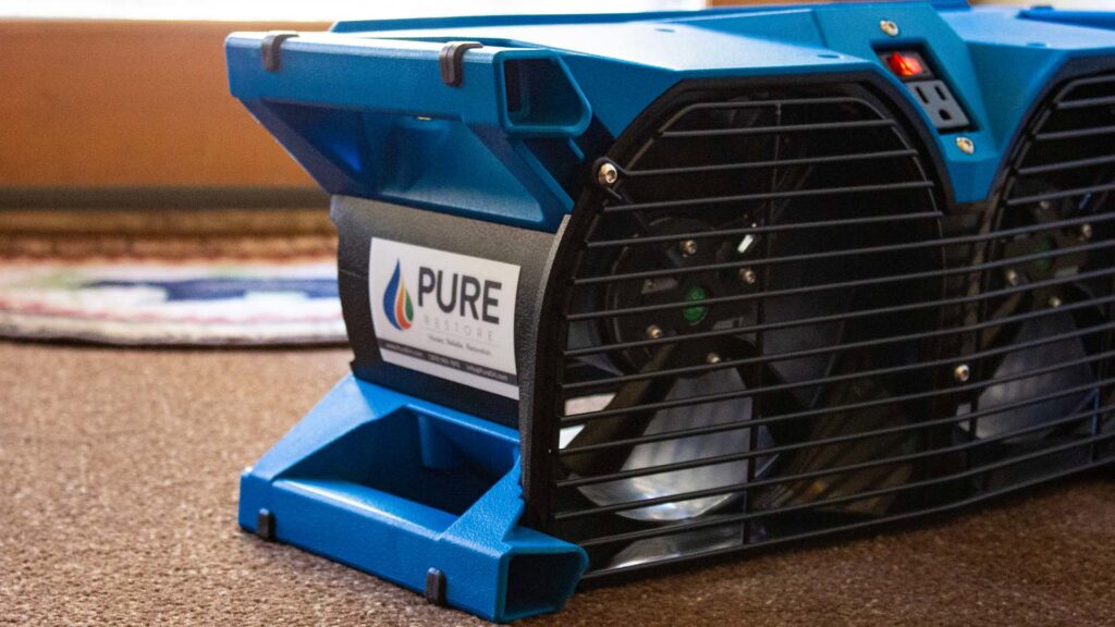 A close-up of a blue industrial air mover fan on a carpeted floor by Pure Restore in Northglenn, CO.