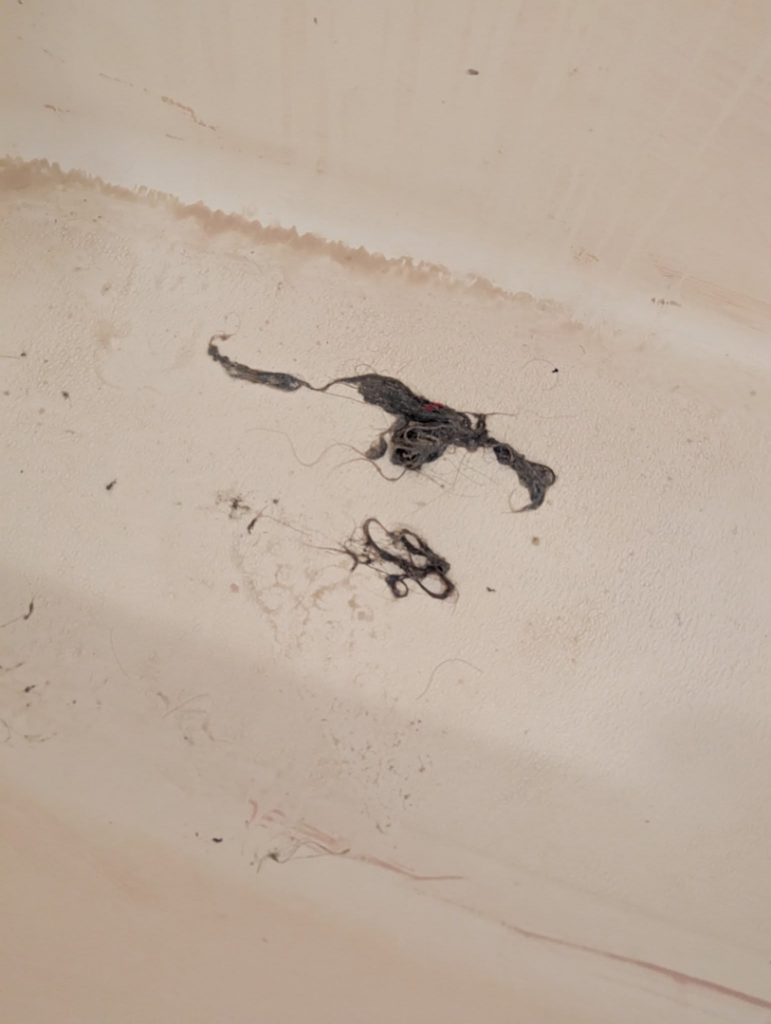 A close-up view of dirt and hair collected in a bathtub, indicating a need for cleaning by The Cleaning Fairy in Fort Lauderdale, FL.