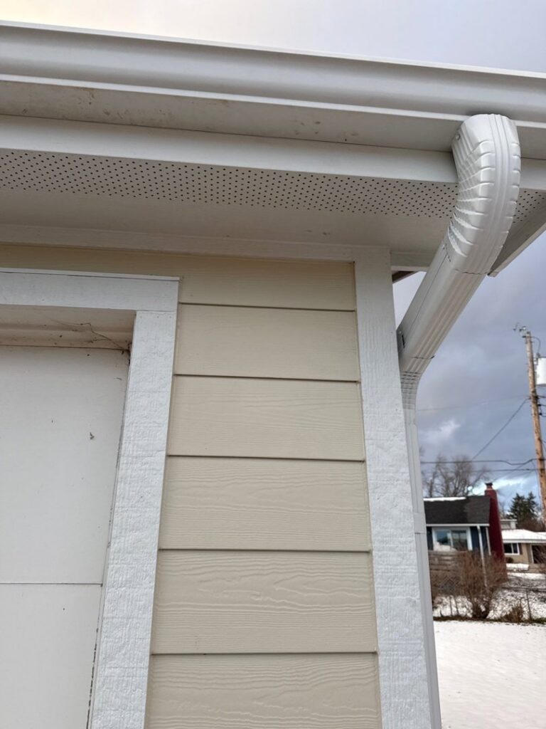 A close-up view of newly installed light beige siding, soffit, and gutter by Bishop Exteriors in Omaha, NE.