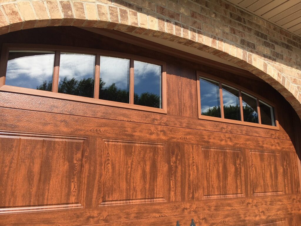 Close-up of a brown wood-grain garage door with arched windows, installed by Elite Door in Winchester, CA.