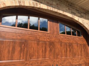 Close-up of a brown wood-grain garage door with arched windows, installed by Elite Door in Winchester, CA.