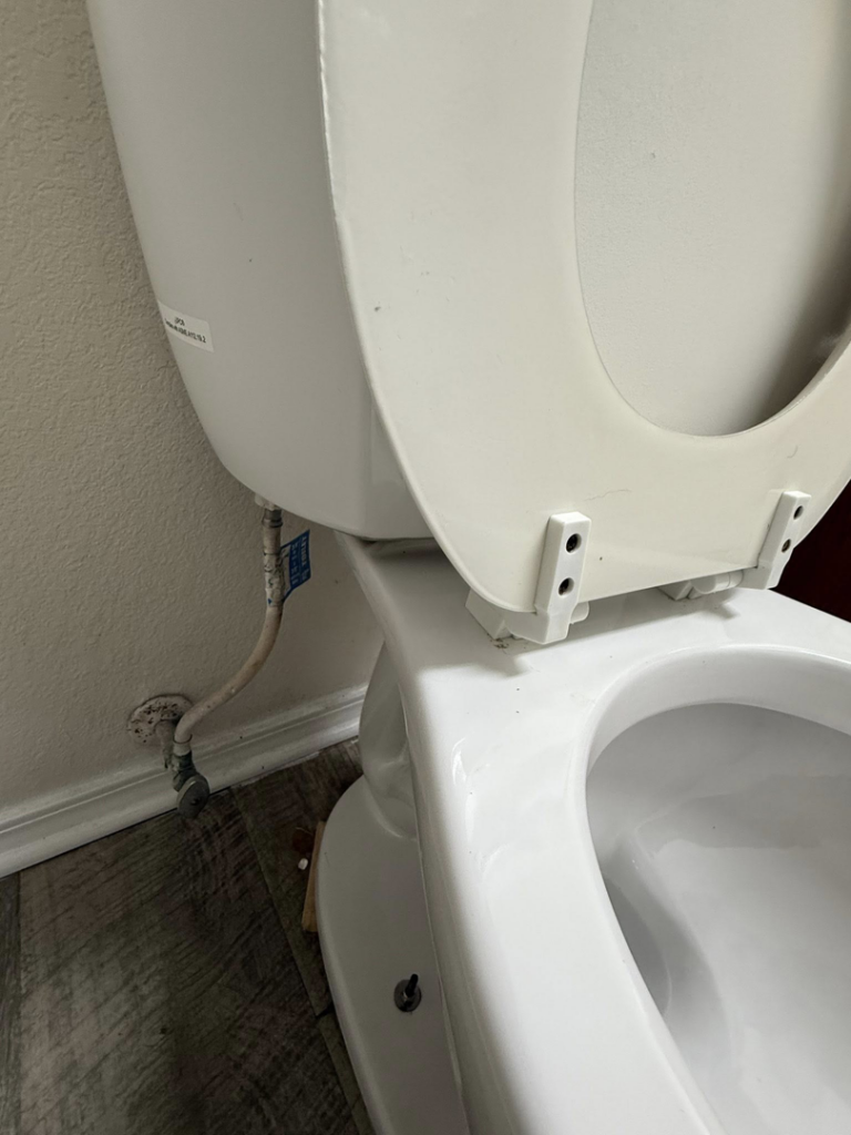 A close-up view of a dirty toilet base and hinges, before professional cleaning by WWJM Cleaning Service in Oklahoma City, OK.
