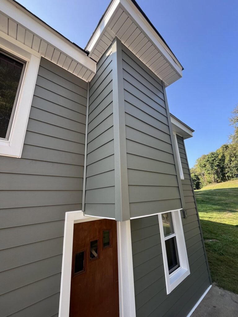 A close-up view of a house corner featuring new green siding and crisp white trim by My Guys Remodeling Experts in Bethel Park, PA.