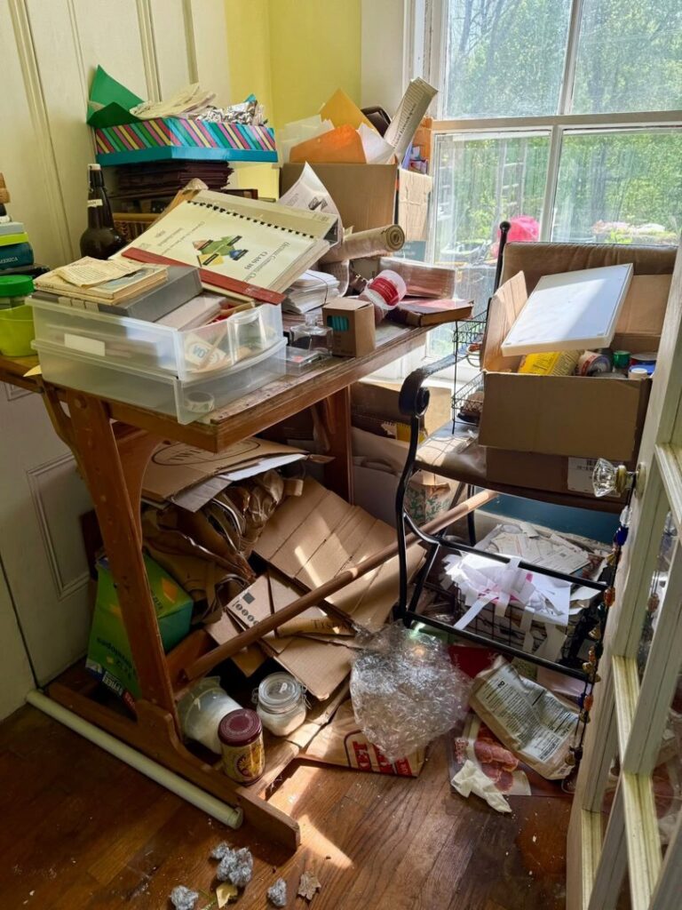 A cluttered home office desk and floor before a professional decluttering service by KDG Decluttering in Manchester, NH.