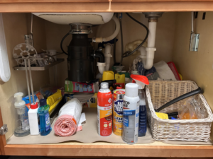 A cluttered cabinet under a kitchen sink before professional cleaning by On Course Cleaning in Fayetteville, NC.