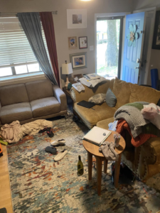 A cluttered living room with clothes and items on the couch and floor, awaiting professional house cleaning from EMarie Professional Cleaning Services & More in Little Rock, AR.