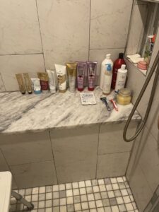 A cluttered shower bench with numerous bottles and toiletries, indicating a need for cleaning and organization by JLJ Sister's Cleaning & More in Lexington, KY.