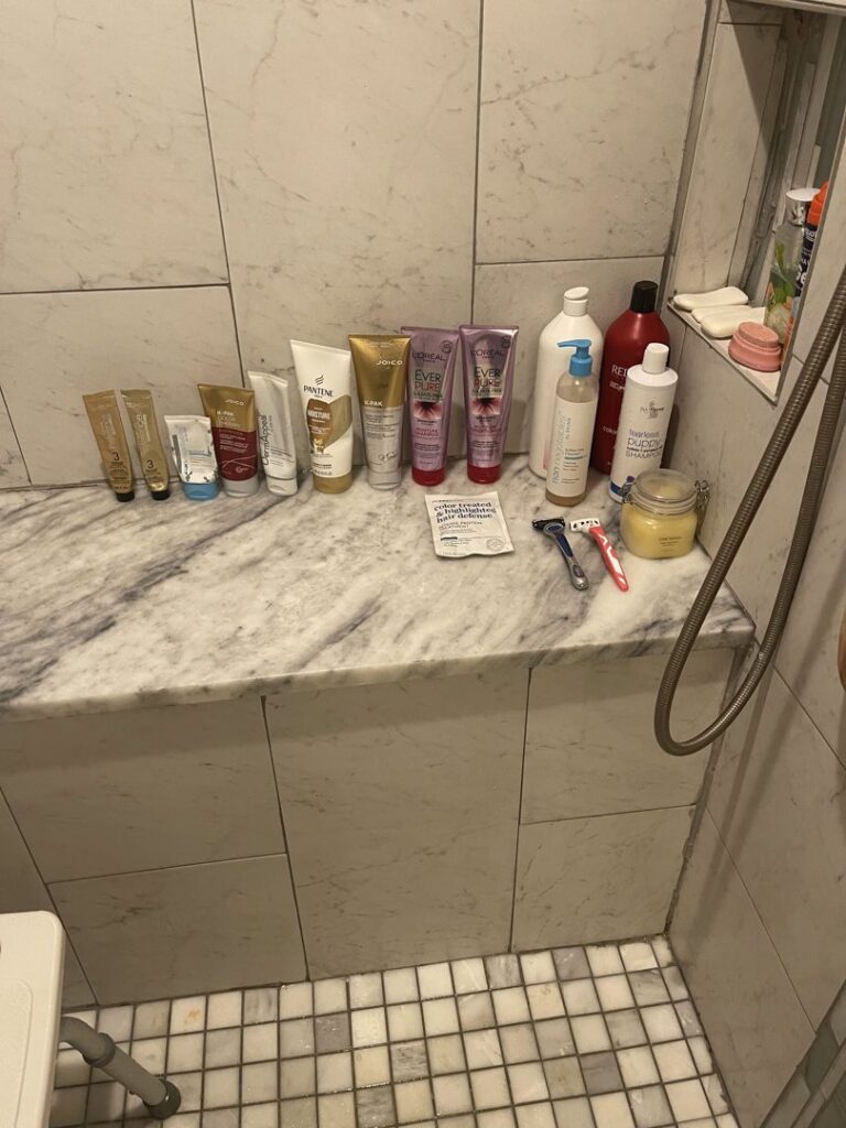 A cluttered shower bench with numerous bottles and toiletries, indicating a need for cleaning and organization by JLJ Sister's Cleaning & More in Lexington, KY.